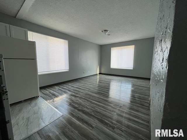 empty room with a textured ceiling, baseboards, and wood finished floors