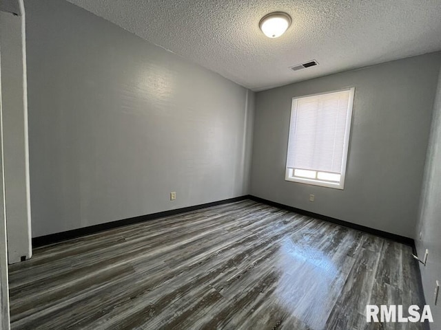 spare room featuring dark wood-style flooring, visible vents, a textured ceiling, and baseboards