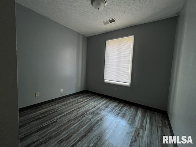 spare room featuring visible vents, dark wood finished floors, a textured ceiling, and baseboards