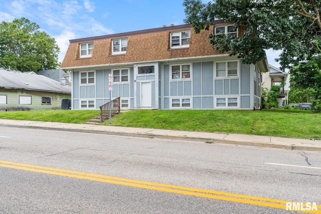 view of front of house with a shingled roof, mansard roof, board and batten siding, and a front yard