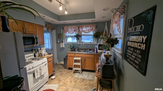 kitchen featuring light tile patterned floors, a raised ceiling, light countertops, a sink, and white appliances