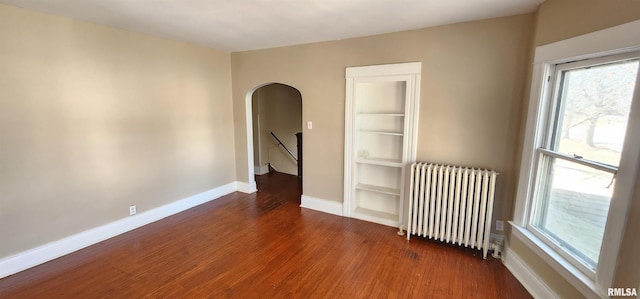 814 W Edwards St, Springfield, IL 62704 - spare room featuring radiator heating unit, arched walkways, wood finished floors, and baseboards
