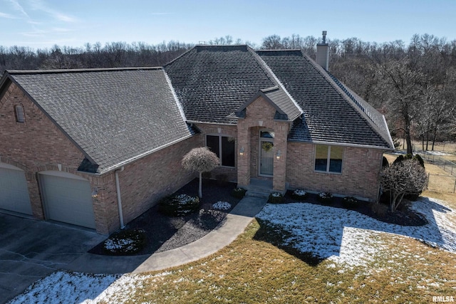 view of front facade featuring driveway, brick siding, a chimney, and an attached garage