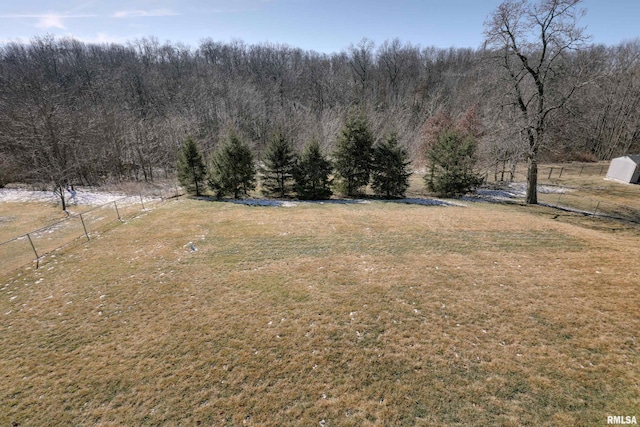 view of yard featuring a rural view, fence, and a wooded view