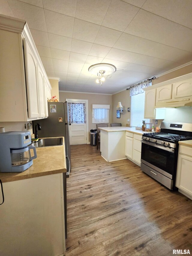 kitchen featuring gas range, a peninsula, crown molding, and wood finished floors