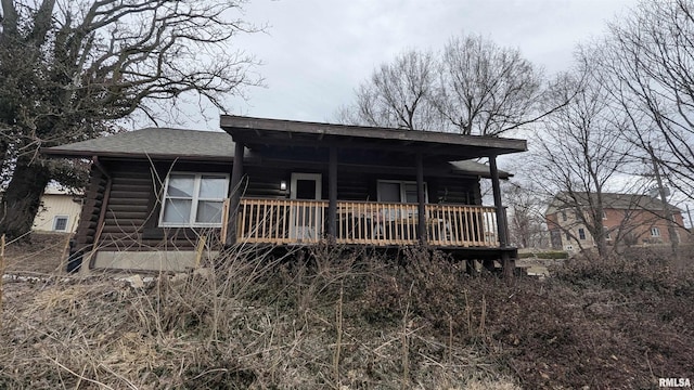 rear view of property featuring a shingled roof, covered porch, and log siding