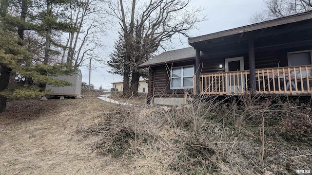 view of side of home with covered porch, roof with shingles, and log siding