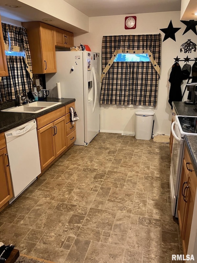 kitchen with dark countertops, brown cabinetry, stone finish floor, a sink, and white appliances