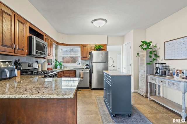 kitchen featuring brown cabinets, stainless steel appliances, backsplash, a sink, and light stone countertops