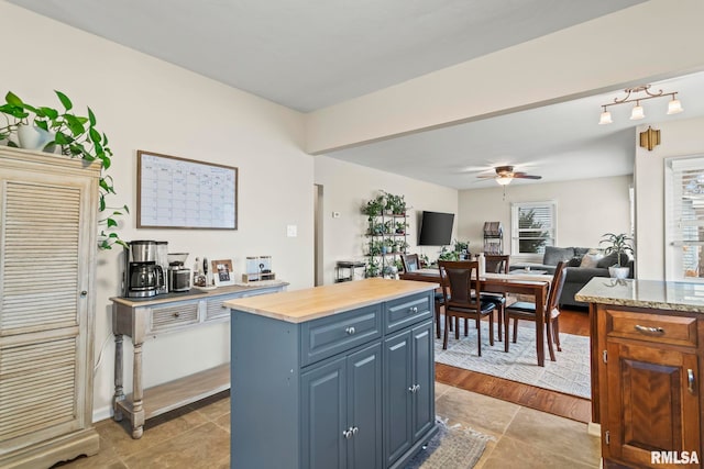 kitchen featuring a ceiling fan, butcher block counters, open floor plan, a center island, and blue cabinets