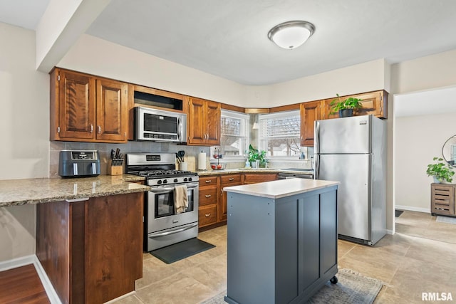 kitchen featuring tasteful backsplash, baseboards, appliances with stainless steel finishes, brown cabinets, and a peninsula