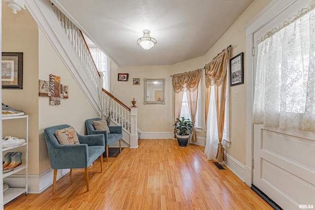 foyer entrance with visible vents, stairway, light wood-style flooring, and baseboards