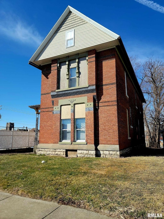 view of front facade with brick siding, a front yard, and fence