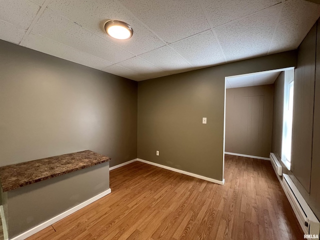 spare room featuring a paneled ceiling, wood finished floors, baseboards, and a baseboard radiator