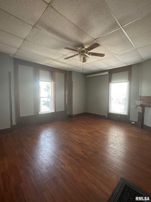 unfurnished living room featuring a wealth of natural light, a paneled ceiling, and wood finished floors