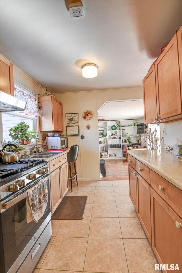 kitchen with light tile patterned floors, a sink, stainless steel gas range, and light countertops