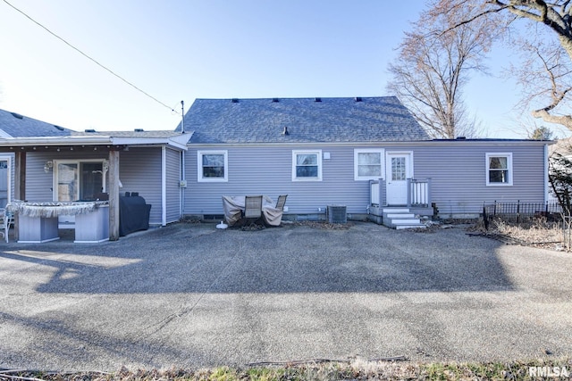 rear view of property featuring central air condition unit and roof with shingles