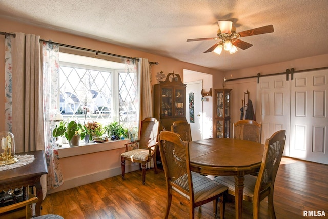 dining space featuring a barn door, a textured ceiling, wood finished floors, and a ceiling fan