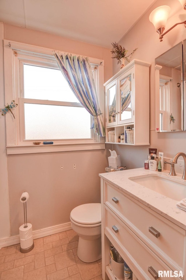 bathroom with a healthy amount of sunlight, toilet, vanity, and baseboards