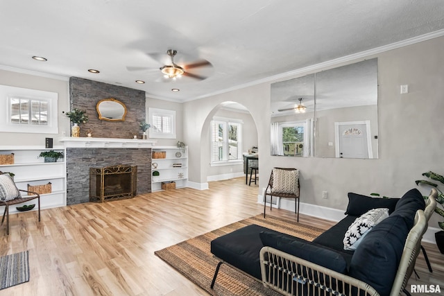 living room featuring ornamental molding, wood finished floors, arched walkways, a fireplace, and baseboards