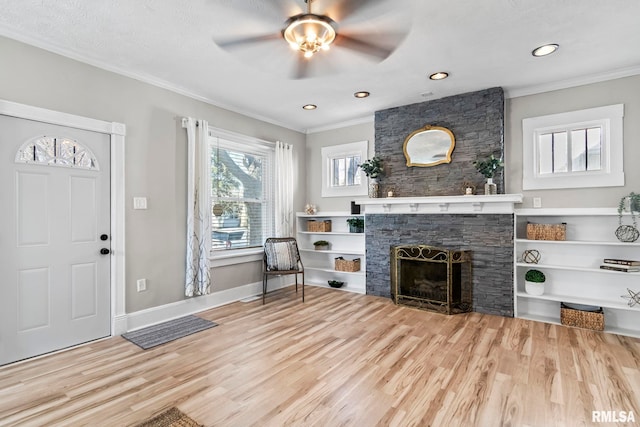 entryway featuring a stone fireplace, crown molding, wood finished floors, and baseboards