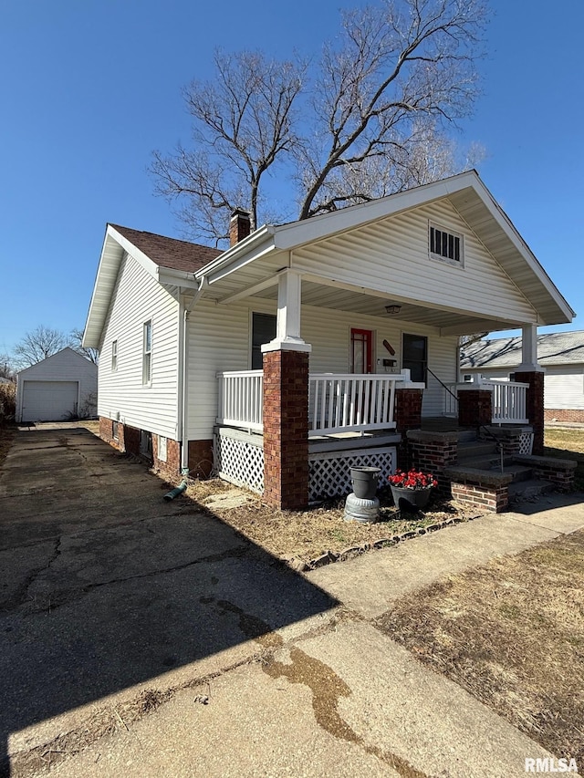 view of front of house with a detached garage, aphalt driveway, covered porch, a chimney, and an outbuilding