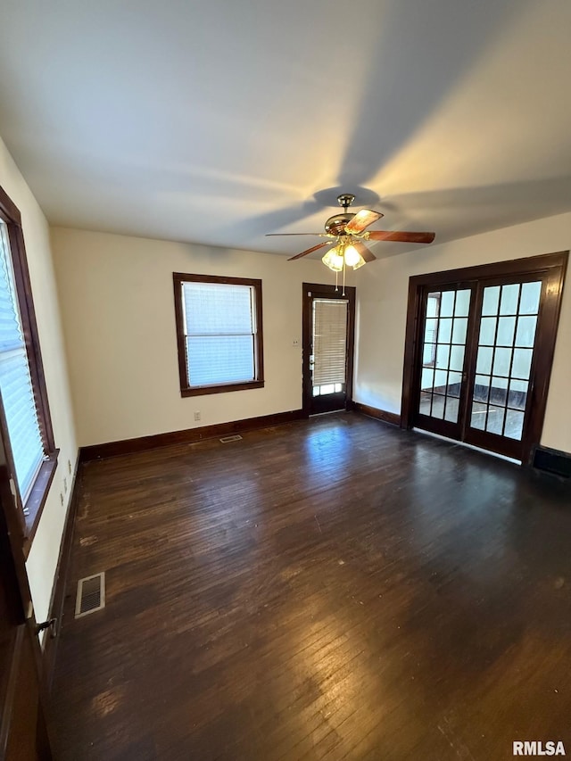 empty room featuring visible vents, a healthy amount of sunlight, dark wood-type flooring, and baseboards