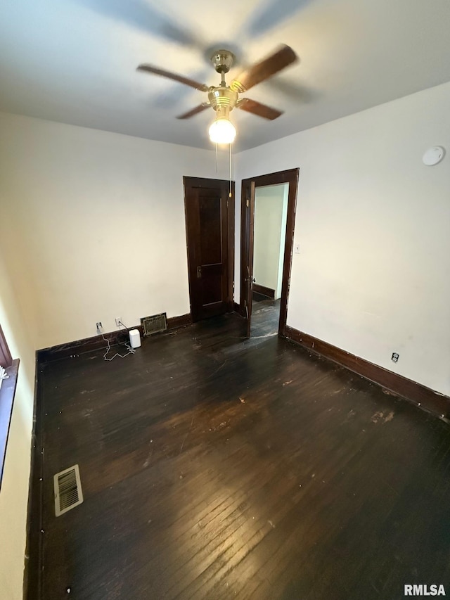 spare room with dark wood-style floors, visible vents, a ceiling fan, and baseboards