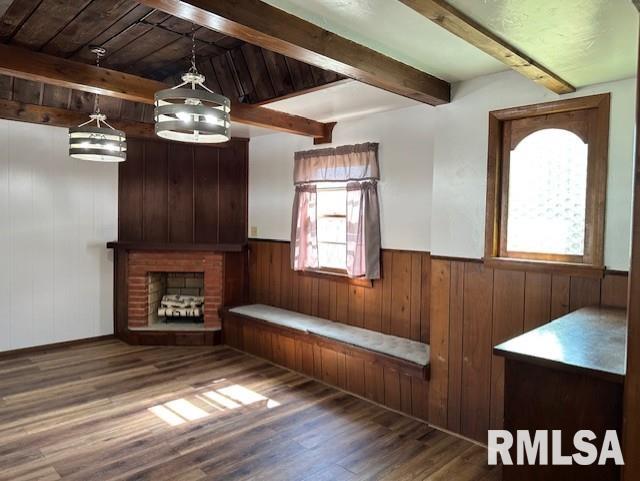 unfurnished living room with beamed ceiling, wood walls, a wainscoted wall, a fireplace, and wood finished floors