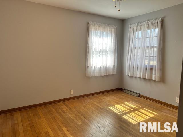 spare room featuring light wood-type flooring, baseboards, a ceiling fan, and a baseboard radiator