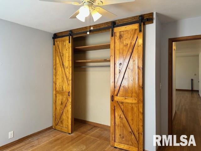 unfurnished bedroom with a closet, baseboards, a barn door, and wood finished floors