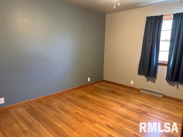 empty room featuring a baseboard heating unit, baseboards, and light wood finished floors