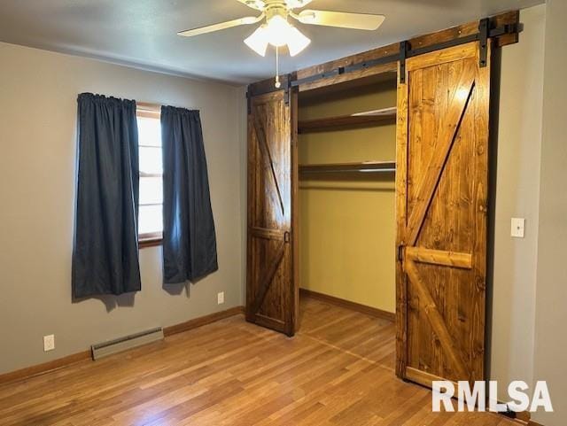 unfurnished bedroom with a barn door, baseboards, baseboard heating, and light wood finished floors