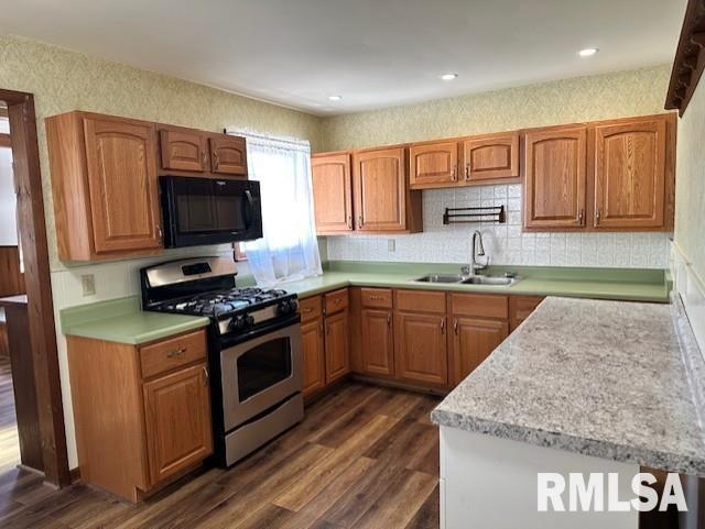 kitchen featuring a sink, dark wood finished floors, black microwave, light countertops, and stainless steel gas range