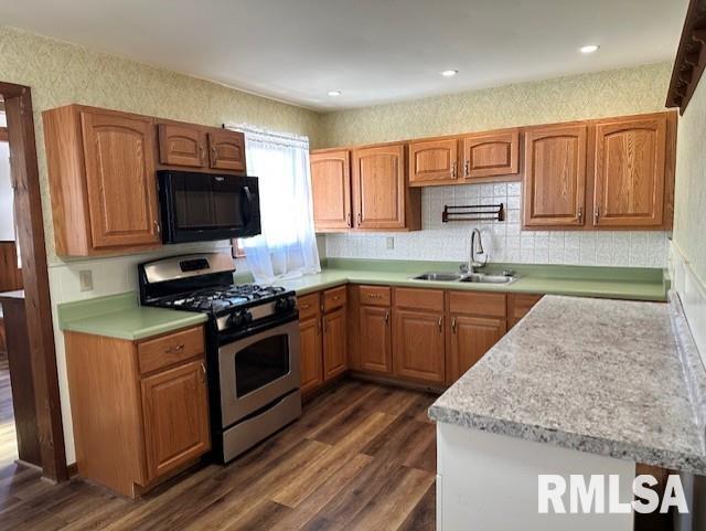 kitchen with stainless steel gas range oven, black microwave, light countertops, dark wood-style floors, and a sink