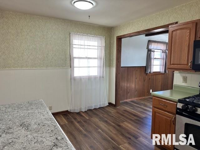 kitchen with light countertops, stainless steel gas range, black microwave, wainscoting, and dark wood-style flooring