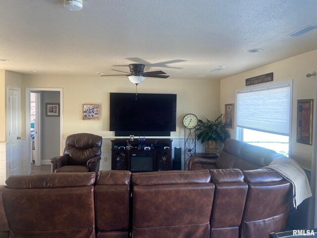 living area with a glass covered fireplace, a textured ceiling, and ceiling fan