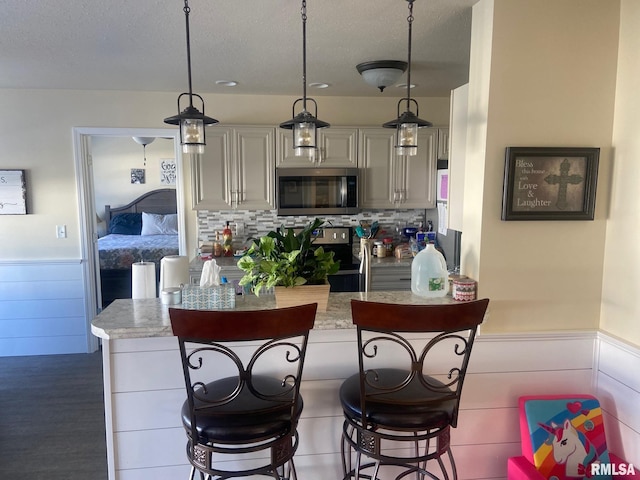 kitchen with a breakfast bar, a wainscoted wall, stainless steel appliances, and light stone counters