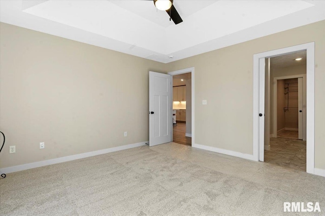 unfurnished bedroom featuring light carpet, a ceiling fan, a tray ceiling, and baseboards