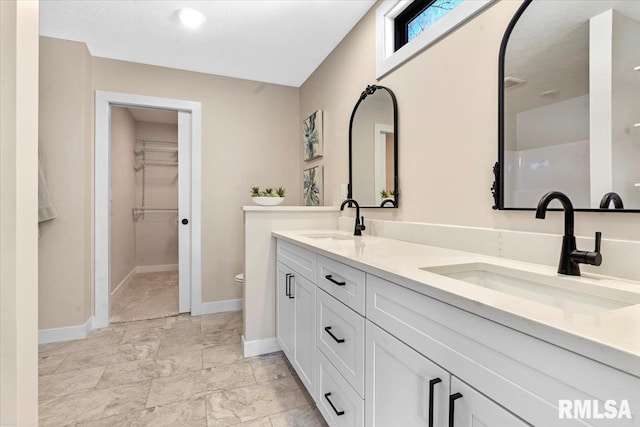 bathroom with a walk in closet, double vanity, baseboards, and a sink