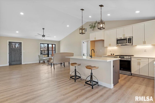 kitchen with a sink, vaulted ceiling, light wood-style flooring, appliances with stainless steel finishes, and a kitchen island with sink