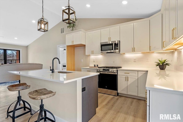 kitchen with lofted ceiling, light wood-type flooring, appliances with stainless steel finishes, and a sink