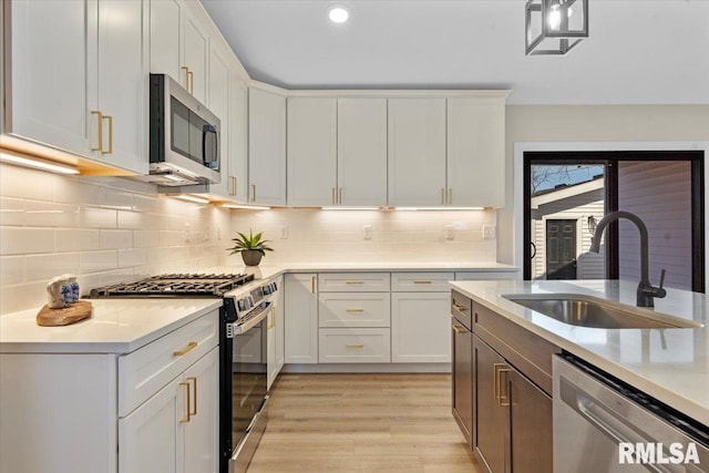 kitchen featuring light wood finished floors, light countertops, appliances with stainless steel finishes, white cabinets, and a sink