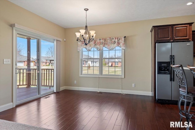 unfurnished dining area featuring dark wood-style floors, plenty of natural light, baseboards, and an inviting chandelier