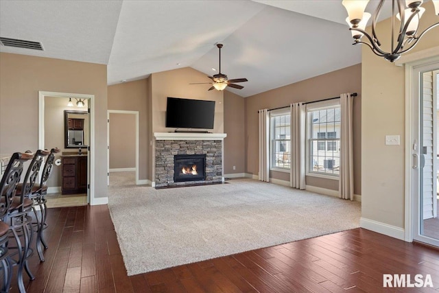 living room with visible vents, dark wood finished floors, lofted ceiling, a stone fireplace, and ceiling fan with notable chandelier