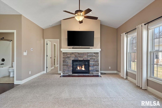 unfurnished living room with a ceiling fan, carpet floors, a stone fireplace, baseboards, and vaulted ceiling