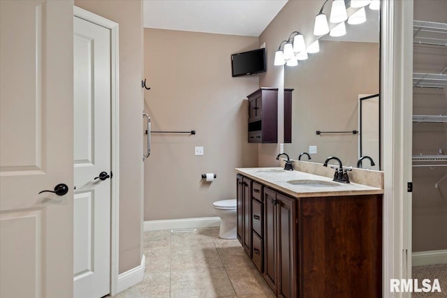 bathroom featuring a walk in closet, double vanity, baseboards, and a sink