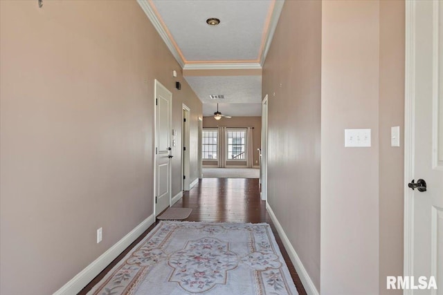 corridor with wood finished floors, visible vents, baseboards, and ornamental molding