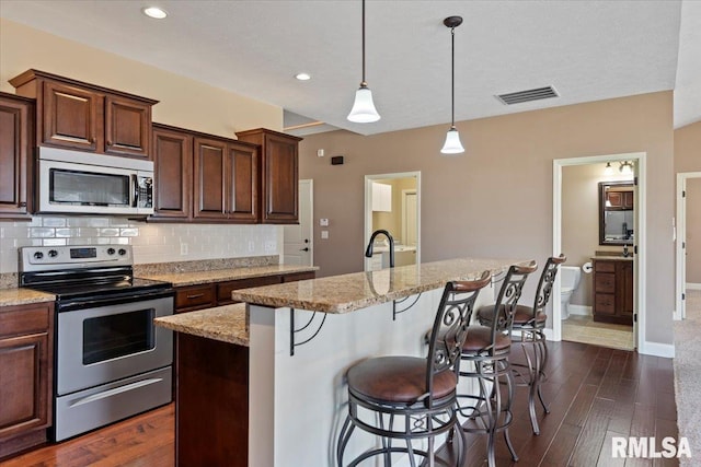 kitchen with visible vents, light stone counters, backsplash, stainless steel appliances, and dark wood-style flooring