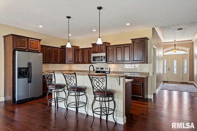 kitchen featuring dark wood-type flooring, a kitchen breakfast bar, tasteful backsplash, stainless steel appliances, and hanging light fixtures